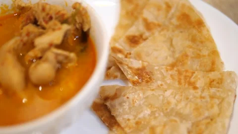 Crispy flatbread roti served with authentic Thai chicken Panang curry Stock Footage 332144713