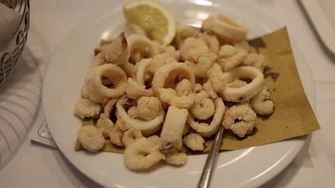 Crispy fried calamari rings served with a lemon wedge on a white plate Stock Footage 328286453