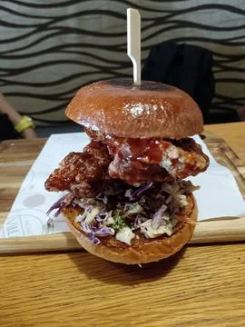 A crispy fried chicken burger features creamy coleslaw, glossy sauce, and a toas Stock Photos