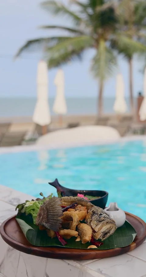 Crispy fried fish served by poolside with ocean view, tropical setting Stock Footage 314044572