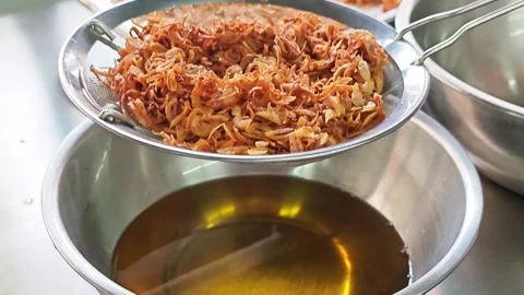 Crispy fried shallots draining in a metal strainer. Video stock 346536728