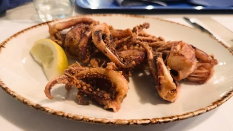 Crispy fried squid served with lemon wedges at a seafood restaurant. These Stock Footage 330607492