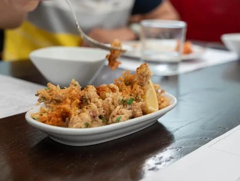 Crispy fried squid tentacles served on a plate with a lemon wedge in a rest.. Фото
