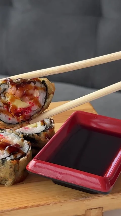 Crispy fried sushi rolls dipped into soy sauce with disposable wooden Stock Footage 346189374