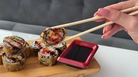 Crispy fried sushi rolls dipped into soy sauce with disposable wooden Stock Footage 346189393