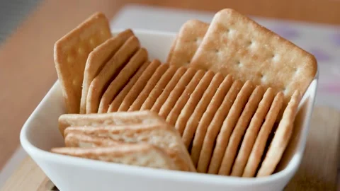 Crispy golden crackers arranged in white ceramic bowl on wooden table, salty Stock Footage 341828900