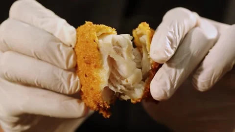Crispy golden fish fillet split in half by gloved hands with hot steam Stock Footage 333775437