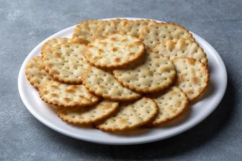 Crispy Golden Salted Water Crackers Stacked on a Ceramic White Plate Foto stock