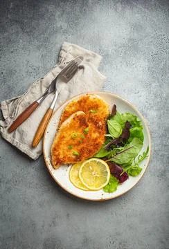 Crispy panko breaded fried chicken fillet with green salad and lemon on plate Foto stock