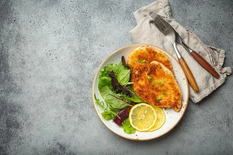 Crispy panko breaded fried chicken fillet with green salad and lemon on plate on Stock-Fotos