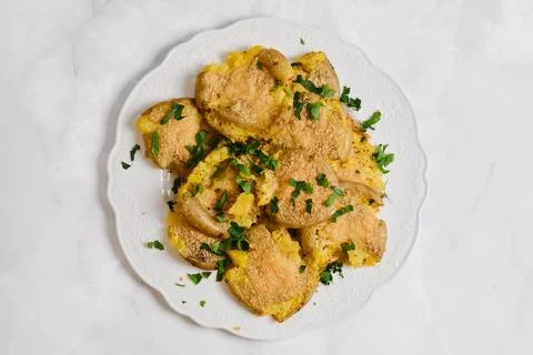 Crispy smashed potatoes served on a white plate with chopped herbs on a lig.. Foto stock
