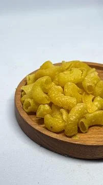 Crispy spicy macaroni snack served on a wooden plate on white background Stock Photos