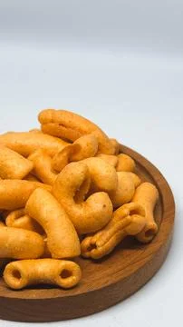 Crispy spicy macaroni snack served on a wooden plate on white background Stock Photos