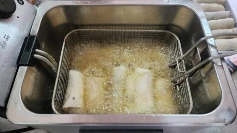 Crispy Spring Rolls Being Deep Fried in Hot Oil Inside an Electric Fryer Bask Stock-Fotos