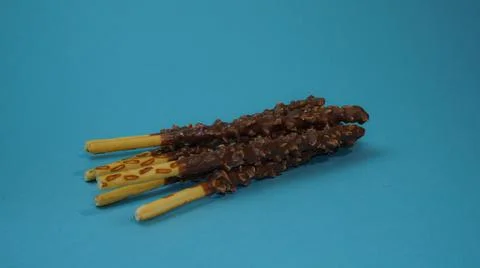 Crispy sticks with hazelnut sprinkles in chocolate on a blue background. Stock Illustration