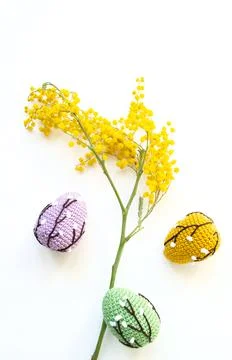Crocheted colored Easter eggs with mimosa on a white background. Top view. Foto stock