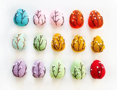 Crocheted colored Easter eggs on a white background lie in a row. Top view. Stock Photos