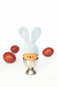 Crocheted Easter egg with bunny ears in an egg holder and painted red eggs on Stock Photos