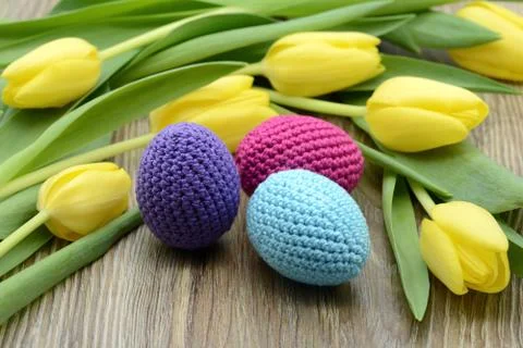 Crocheted easter eggs and  a bouquet of yellow tulips. Stock Photos