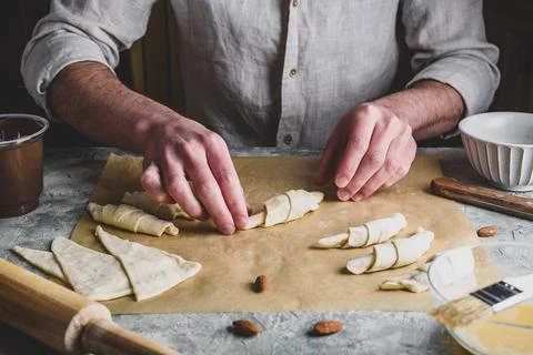 Croissant preparing. Baker rolls the puff pastry stuffed with almonds and spr Stock Photos