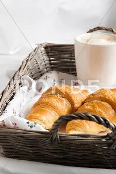 Croissants, coffee cup, flower in romantic style on a wicker tray on white be Stock Photos