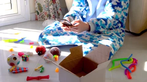 Crop anonymous kid in soft pajama sitting on floor surrounded by colorful toy Stock Footage 167141680
