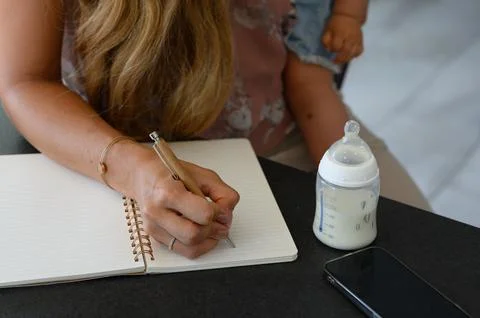 Crop anonymous working mom taking notes in notebook and hugging baby Stock Photos