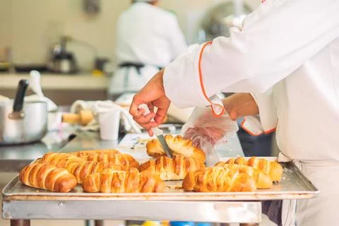 Crop baker checking buns with knife Stock Photos