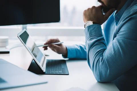 Crop businessman using stylus while browsing tablet placed on keyboard Stock Photos