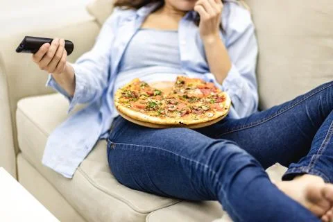 Crop. Close up legs in jeans. Pretty woman is laying on the sofa at home and is Stock Photos