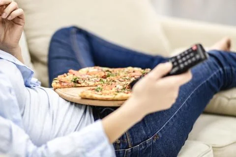 Crop. Close up remote control device. Unrecognizable woman is laying on the sofa Stock Photos