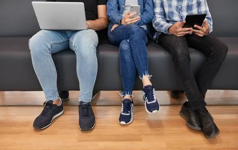 Crop friends using devices in lobby Stock Photos