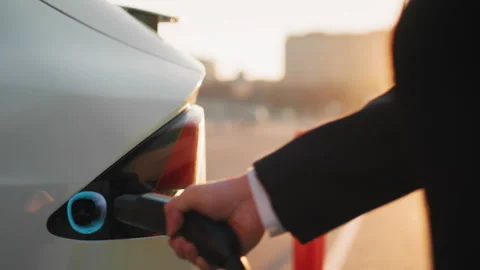 Crop of male hand inserting charging cable into white electric car at outdoors Stock Footage 245258107