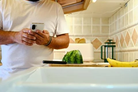 Crop man standing and checking messages on smartphone in kitchen Stock Photos