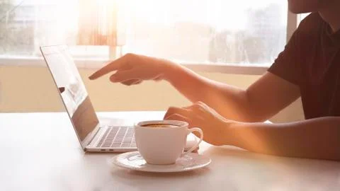 Crop of man's hand points and works on computer in front of a window with cof Stock Photos