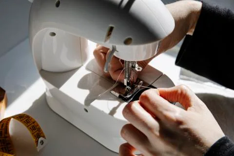 Crop seamstress threading a sewing machine needle at home workshop Stock Photos