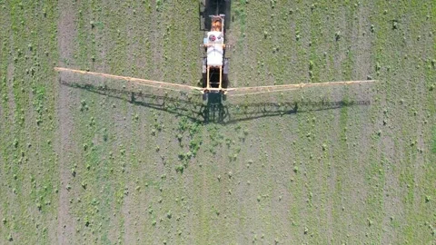 The crop sprayer is actively applying chemicals to the green field below Stock Footage 329320111