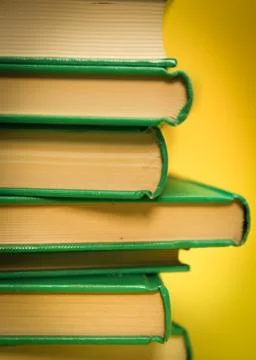 Crop of a vertical stack of books. Yellow background and green books. Stock Photos