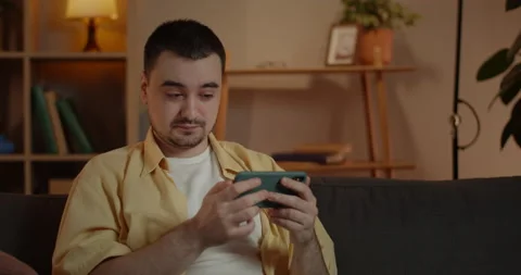 Crop view of concentrated man watching video while sitting on sofa in evening at Video stock 149353237