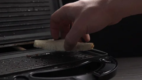 Crop view of man cooking toasts of white bread in electric grill at table Vidéo 104100601