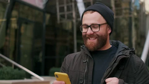 Crop view of man in glasses looking at phone screen and smiling while walking at Video stock 139768652