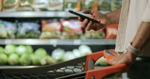 Crop view of man hand holding smartphone and srolling screen in supermarket. Guy Stock Footage 129756446