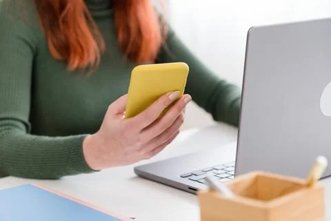 Crop woman using smartphone while working on laptop Stock Photos
