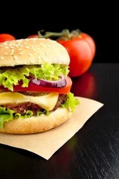 Cropped big cheeseburger on paper on wooden black desk Stock Photos