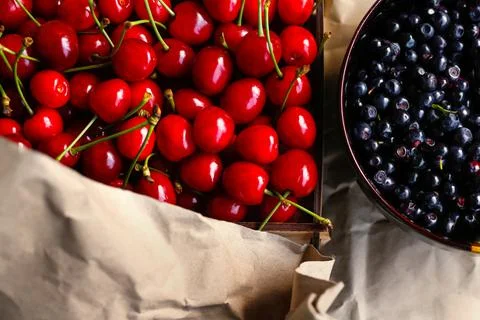 Cropped box, crape of dark red sweet cherries with tail and bowl of blueberri Foto stock