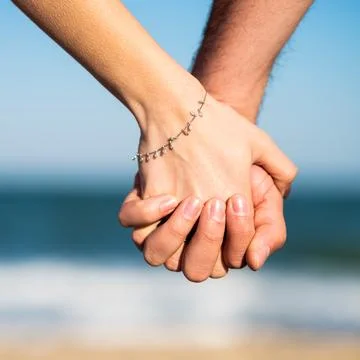Cropped close up back view of a couple holding each other's hands at the beac Stock Photos