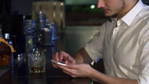 Cropped close up of a man using his smart phone at the bar while having a drink Video stock 84685184