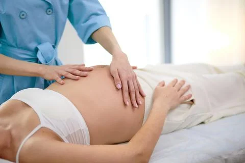 Cropped female physiotherapist doing belly massage to beautiful pregnant woman Stock Photos