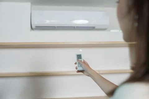 Cropped hand holding remote control to adjust air conditioner temperature at Фото