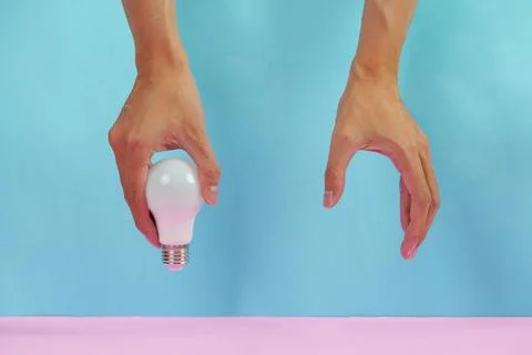 Cropped hands holding LED light bulb on blue and pink background for idea Stock Photos